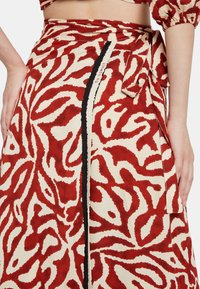 Falda envolvente de lino con un patrón abstracto rojo y beige, cinturilla atada y un acento negro a lo largo del lado. Textura ligera.