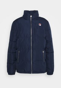 Mörkblå puffjacka med hög krage, framdragkedja och dragkedjefickor på sidorna. Har en liten logotyp på bröstet. Tillverkad av vadderat tyg.