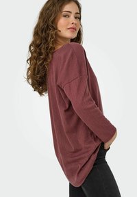 Maglia a maniche lunghe color bordeaux con un motivo a coste testurizzato, vestibilità comoda e spalle scese, abbinata a jeans scuri.