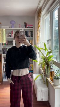 Čierna skrátená mikina s kapucňou a sťahovacou šnúrkou, skombinovaná s červenými károvanými širokými nohavicami. Oblečenie má hladkú textúru a voľný strih.