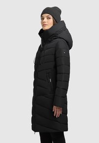 Sort polstret frakke med høj krave og stor hætte, der har lynlåslommer og et slankt, forlænget design. Glat, mat tekstur.
