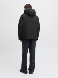 Μαύρο κ jacket με κουκούλα και κομψό σχέδιο, με ματ φινίρισμα. Συνδυάζεται με φαρδιά σκούρα γκρι παντελόνια και ανθεκτικά μαύρα παπούτσια.