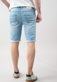 Pantalones cortos de mezclilla azul claro con puños enrollados, que cuentan con dos bolsillos traseros con detalles de costura. Combinados con zapatillas grises y blancas.