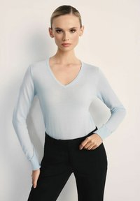Jasnoniebieski, długi rękaw sweter w serek, wykonany z miękkiego materiału, w połączeniu z czarnymi obcisłymi spodniami. Sweter ma subtelną teksturę i ściągacze na mankietach.