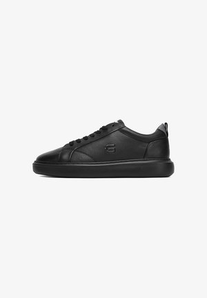 Zapatilla baja de piel negra con puntera redonda, cierre de cordones, superficie texturizada, logo en el lateral y suela gruesa de goma.
