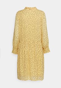 Robe jaune à manches longues, avec une taille froncée et des pois noirs sur toute la surface. Texture semi-translucide et détail de col.