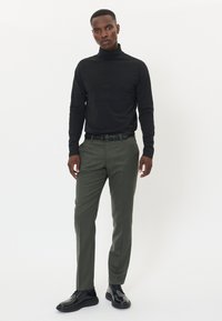 Svart polotröja, slim-fit olivgröna byxor och svarta snörskor. Modern design med slät textur och skräddarsydd passform.