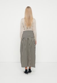 Lang skjørt med vertikale svart-hvite striper, tettsittende midje, sammen med en lys beige langermet topp og svarte sneakers.