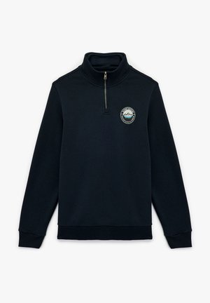 Sudadera de zip de media longitud en color navy, fabricada con tela suave, que presenta un parche redondo con un diseño de montaña en el pecho y puños y dobladillo acanalados.