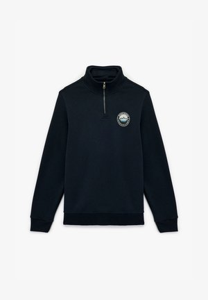 Sudadera de zip de media longitud en color navy, fabricada con tela suave, que presenta un parche redondo con un diseño de montaña en el pecho y puños y dobladillo acanalados.