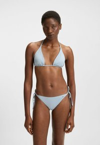 Set di bikini azzurro chiaro realizzato in tessuto morbido; top alla halter con coppe triangolari e slip bikini con laccetti laterali, dotato di un piccolo etichetta del marchio.