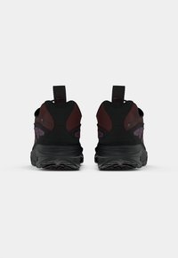Par tenisice Nike u crnoj i tamnocrvenoj boji od Gore-Tex-a, snimljene s leđa, prikazujući petne ručke i teksturirane potplate.