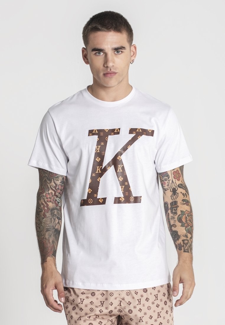 Bílý bavlněný tričko se velkým hnědým grafickým písmene "K" se vzorem log. Krátké rukávy a klasický kulatý výstřih.