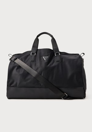 Grand sac de sport noir avec deux poignées courtes, une bandoulière réglable et un petit logo triangulaire Guess au centre avant.