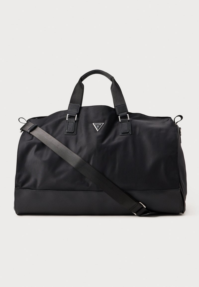 Grand sac de sport noir avec deux poignées courtes, une bandoulière réglable et un petit logo triangulaire Guess au centre avant.