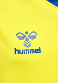 Gul stof med en glat tekstur, der har et blåt Hummel-logo bestående af et bi-lignende design over ordet "hummel" i fede blå bogstaver.