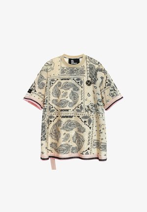 Camiseta beige oversize con estampado de bandana paisley en negro, rayas rosas y negras en las mangas y el bajo, y escote redondo.