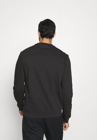 Schwarzes Sweatshirt mit Rundhalsausschnitt, langen Ärmeln und gerippten Bündchen. Glattes Material, einfaches Design, minimale Details und lässige Passform.