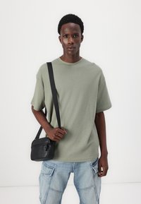 Ljust grönt texturerat oversized t-shirt med rund hals, i kombination med ljusblå cargo-jeans. Svart crossbody-väska med framficka med dragkedja.