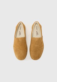 Zapatos de ante marrón tipo slip-on con punta redonda, que presentan patrones de costura diagonal y acentos elásticos en los lados para facilitar su uso.