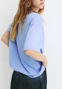 Tricou scurt cu mânecă scurtă, de culoare albastră deschisă, dintr-un material moale, cu un croi lejer și decolteu rotund, asortat cu o pereche de pantaloni mulați din denim închis.