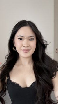 Noor naine, kellel on pikad tumedad juuksed, kannab rõngaskõrvarõngaid ja musta särk, naeratades kaamerasse ühetaolise heleda tausta ees.