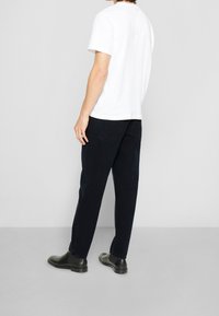 Vit bomulls-T-shirt, avslappnad passform, kombinerad med marinblå denimbyxor och svarta ankelskor. Bakvy, enkel textur, minimalistisk design.