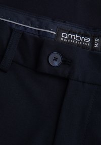 Zwarte stoffen broeken met een gladde textuur, voorzien van een knoopsluiting en een strakke tailleband. Het label toont "ombre quintessence", maat M/32.
