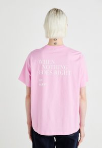 Camiseta de algodón rosa con texto blanco en la parte posterior: "CUANDO NADA SALE BIEN / VE HACIA LA IZQUIERDA." Con mangas cortas y corte relajado.