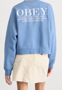 Blå kortärmad sweatshirt med vit tryckt text på baksidan, med stadnamn. Matchad med en beige denimkjol med fickor.