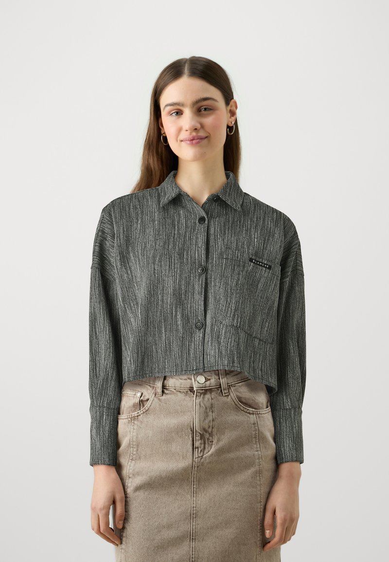 Camisa abotoada cortada em preto e cinza com um padrão texturizado e bolso no peito; combinada com uma saia de ganga castanha clara.