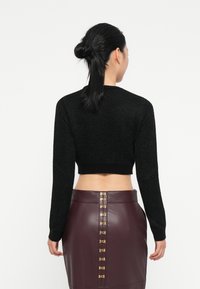 Μαύρος πλεκτός κοντός σκούφος με μακριά μανίκια, διαθέτει υφή και ριμπ τελείωμα. Συνδυάζεται με μια μπορντό φούστα από τεχνητό δέρμα με χρυσές λεπτομέρειες.