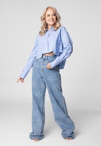 Een geknipte blauw-wit gestreepte overhemd met lange mouwen, gecombineerd met lichtblauwe wijde jeans met sterpatronen.