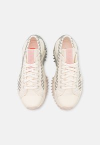 Paire de baskets à lacets de couleur crème avec des rayures grises texturées et des semelles épaisses, vues de dessus sur fond blanc.