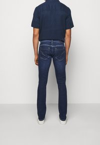 Vaqueros de mezclilla azul oscuro con corte slim, que cuentan con bolsillos traseros con cremalleras y costuras en contraste, combinados con una camisa de manga corta color marino.