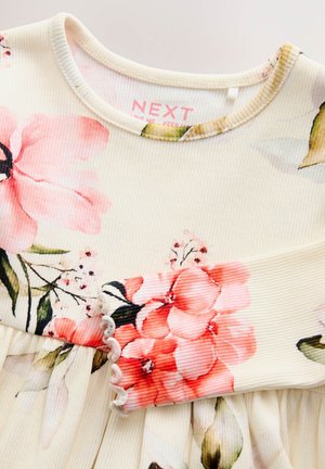 Robe fleurie avec des motifs floraux rose et crème sur un tissu côtelé. Caractérisée par un col rond et un bord festonné aux manches.