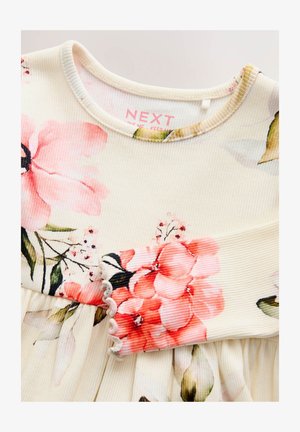 Robe fleurie avec des motifs floraux rose et crème sur un tissu côtelé. Caractérisée par un col rond et un bord festonné aux manches.