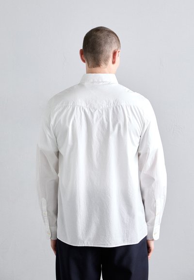 Camisa blanca de manga larga con puños abotonados, con una textura suave y un sutil fruncido en la parte de atrás. Diseño liso, sin patrones.