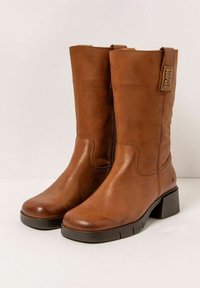 Botas de cuero marrón hasta la rodilla con puntera redondeada, tacón cuadrado y costuras laterales. Presentan un lazo en la parte superior para tirar y un detalle de logo grabado.