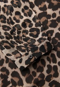 Bluzka w panterkę o plisowanej fakturze, z odcieniami beżu i brązu oraz czarnym guzikiem przy mankiecie.