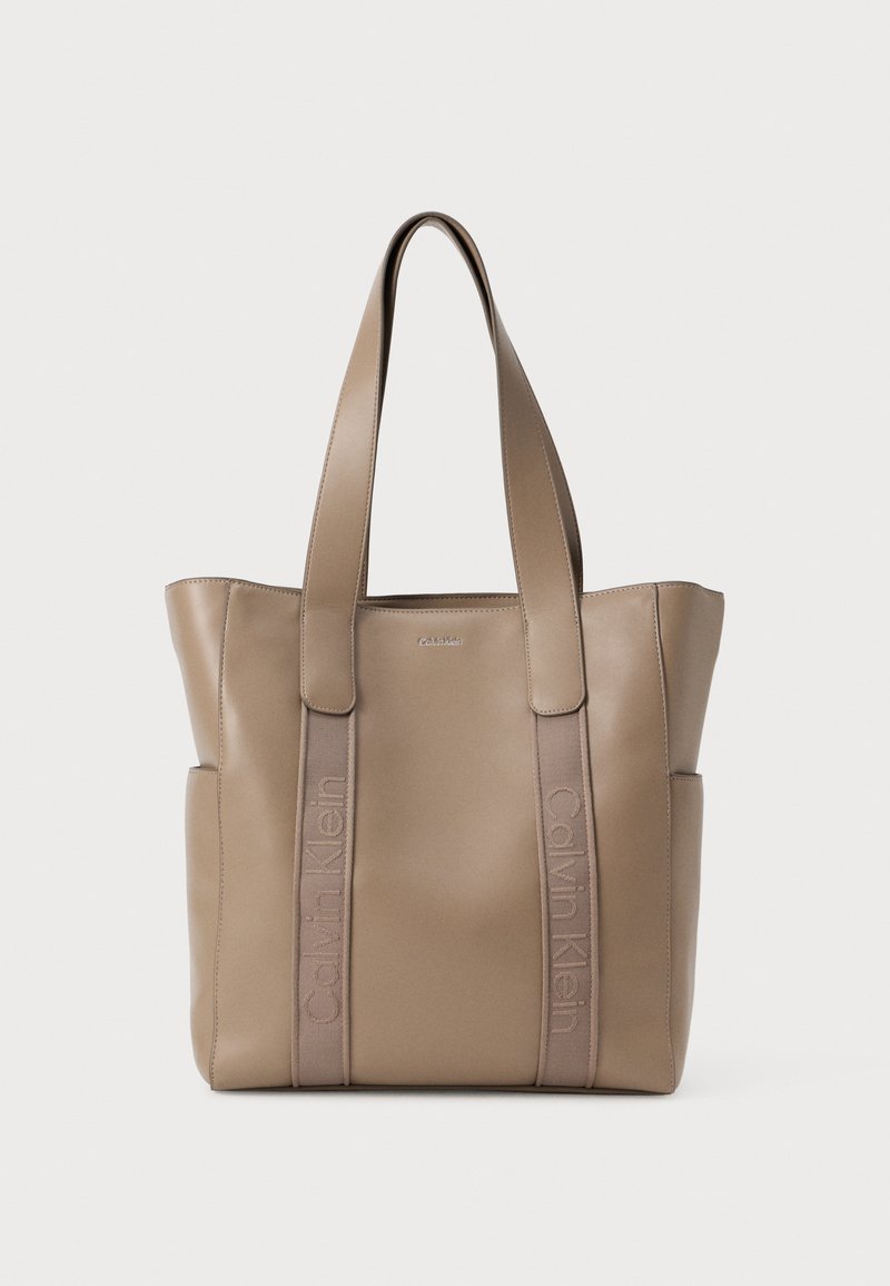 Beige tote taske lavet af glat syntetisk materiale, med to robuste skulderremme og prægning af "Calvin Klein" tekst på siderne.