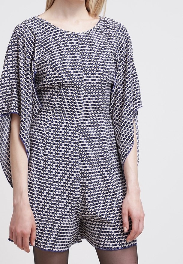 Tyrkysový a bílý vzorovaný overal s volánovými rukávy; má kulatý výstřih, viditelné knoflíky a pohodlný střih. Hladká textura látky.