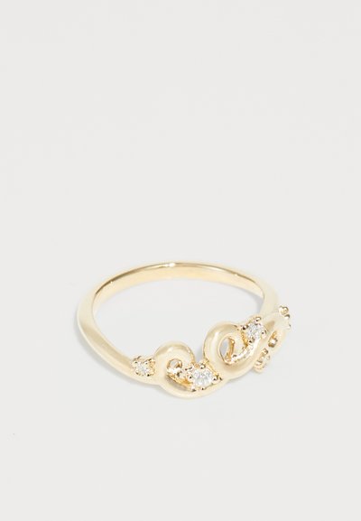 Anillo de metal en tono dorado con un diseño retorcido, adornado con tres piedras preciosas transparentes, textura suave y acabado pulido.