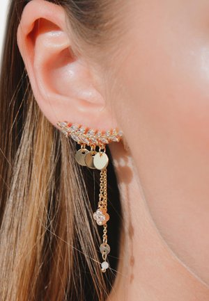 Goldfarbener Ohr-Cuff mit floralem Design, klaren Rhinestones, hängenden goldenen Kreisen und Ketten, vor einem natürlichen Hauthintergrund.