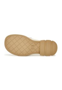 Semelle en caoutchouc d’une chaussure beige avec un motif en losange pour l’adhérence et trois sangles en caoutchouc nervurées près du talon.