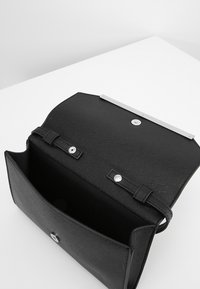 Schwarze strukturiert Lederhandtasche mit silbernem Beschlag, ausgestattet mit einem Klappenverschluss und einem Innenfach. Keine sichtbaren Muster oder Akzente.