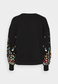 Sweatshirt noir avec manches surdimensionnées ornées de broderies florales colorées et accents blancs. Poignets et col côtelés. Texture de tissu douce.