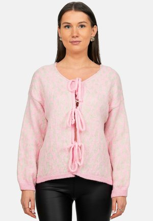 Woman wearing a pink fuzzy cardigan with light animal print and three front tie closures, paired with black fitted pants.
