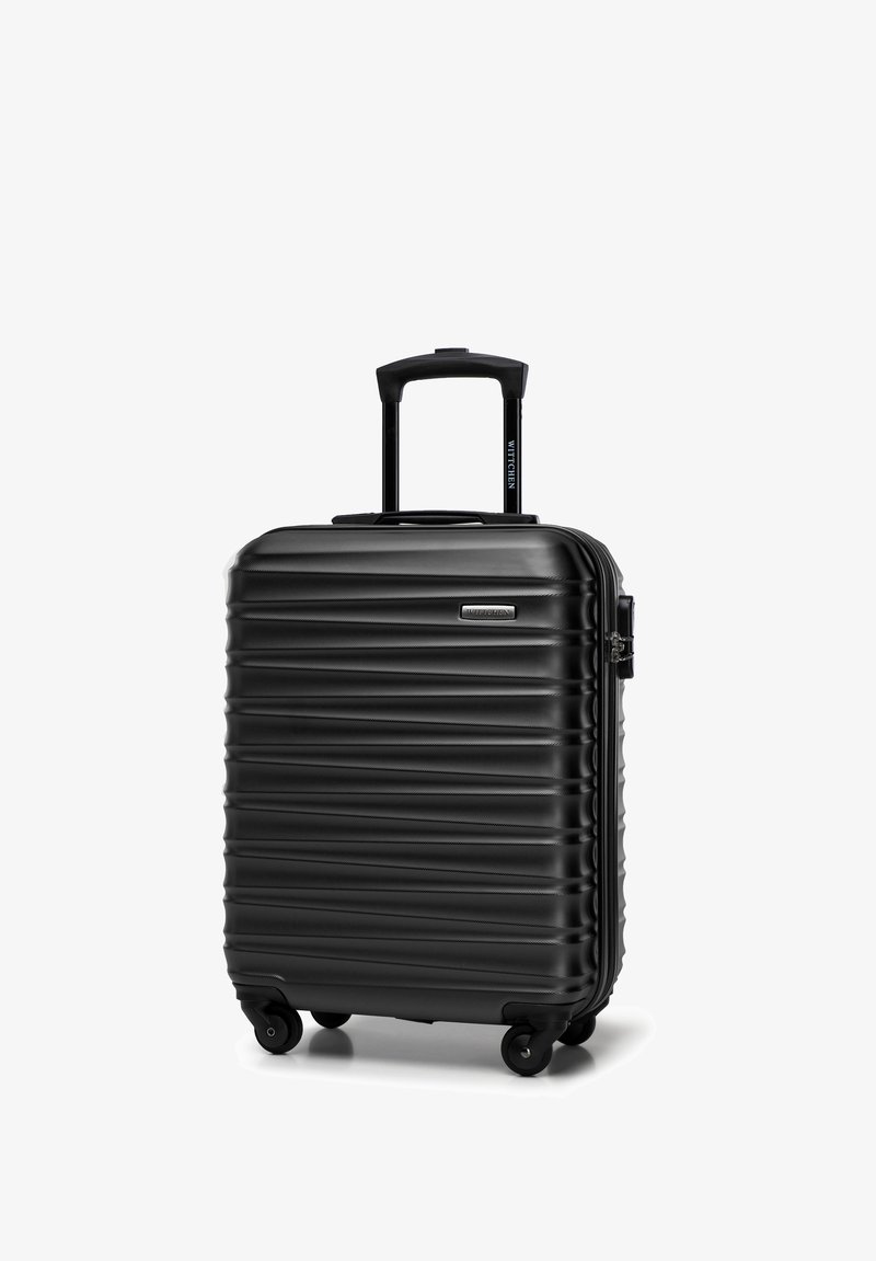 Valigia rigida nera con texture a coste verticali, manico retrattile e quattro ruote per la mobilità. Presenta una chiusura con zip resistente.