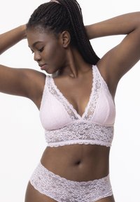 Brassière en dentelle rose pâle avec un décolleté en V profond, ornée de motifs floraux et dotée de bretelles ajustables, accompagnée d'une culotte en dentelle assortie.